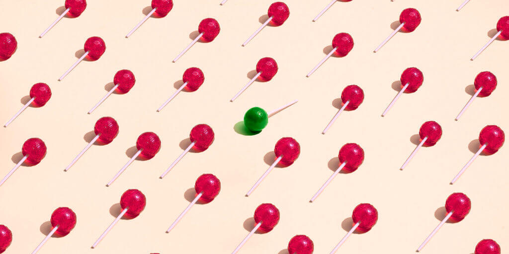 large group of red lollipos placed in a pattern where a green lollipop is standing out from the crowd
